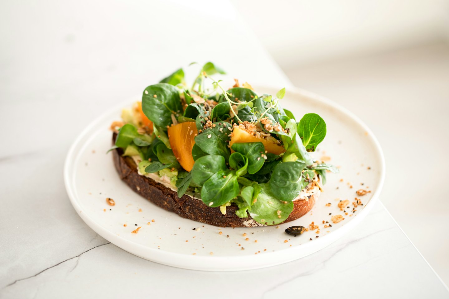 Sándwich abierto con ensalada, caqui y semillas en un plato blanco.