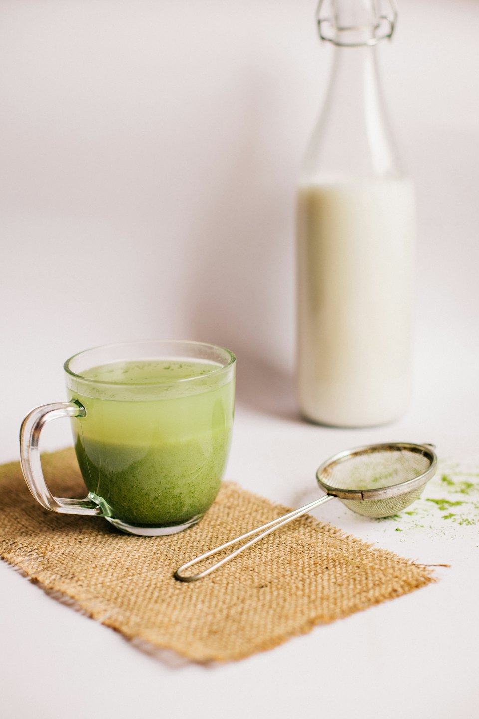 Un latte de matcha en capas en una taza de vidrio sobre arpillera.