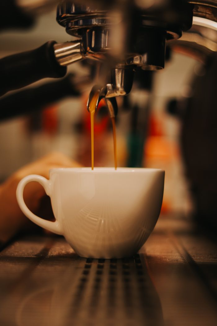Close-up of fresh espresso shot being poured into a white cup from a coffee machine.